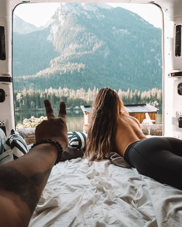 A woman enjoys a peaceful view from a campervan overlooking a serene lake and mountains.