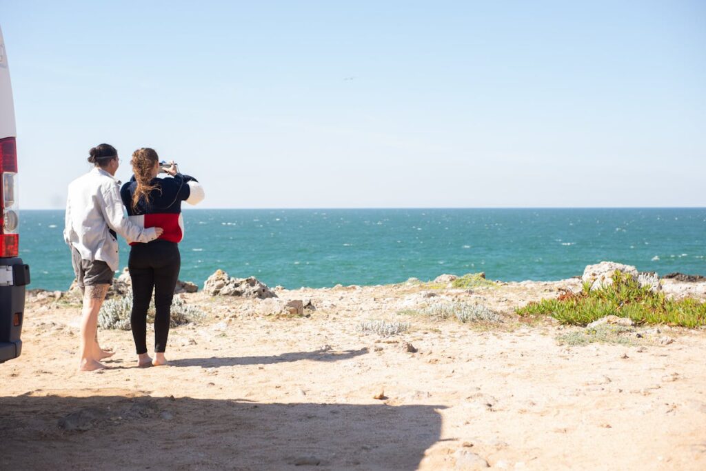 A couple stands by their camper van, capturing the ocean view on a sunny day in Portugal.