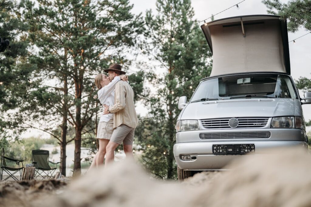 A couple shares an intimate moment near a camper van in a picturesque forest campsite.