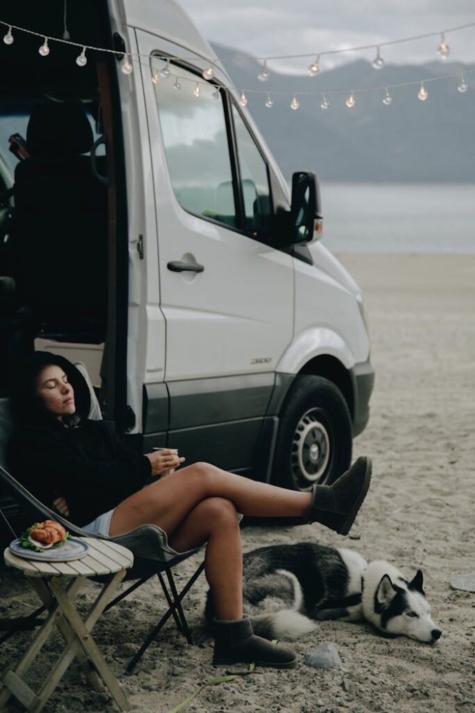Woman enjoys a serene day camping by the beach with her Husky and campervan.