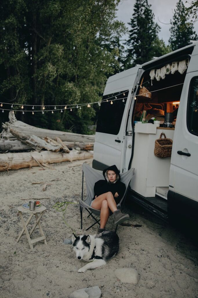 Woman relaxing by campervan with husky dog, enjoying nature outdoors.